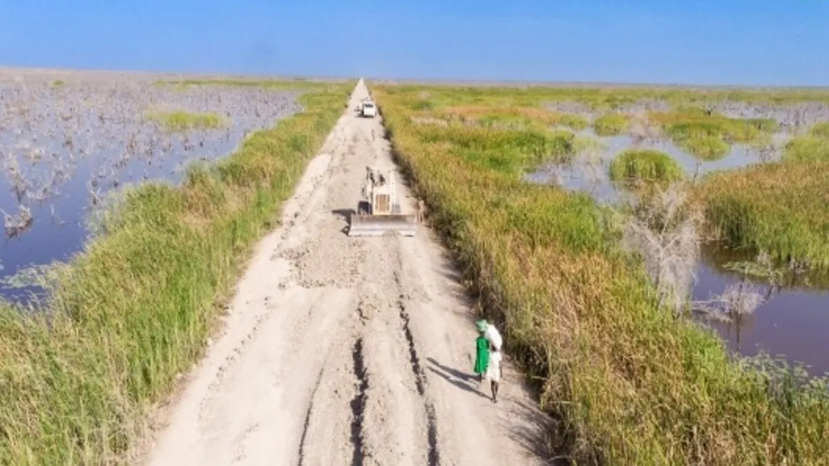 Maintaining the vital but often flood-affected road between Bentiu and Leer is a daunting task. Fortunately, our Pakistani engineers are up to it. An aerial view of a dirt road with grass and bodies of water on either side. On the road, there are some people walking.