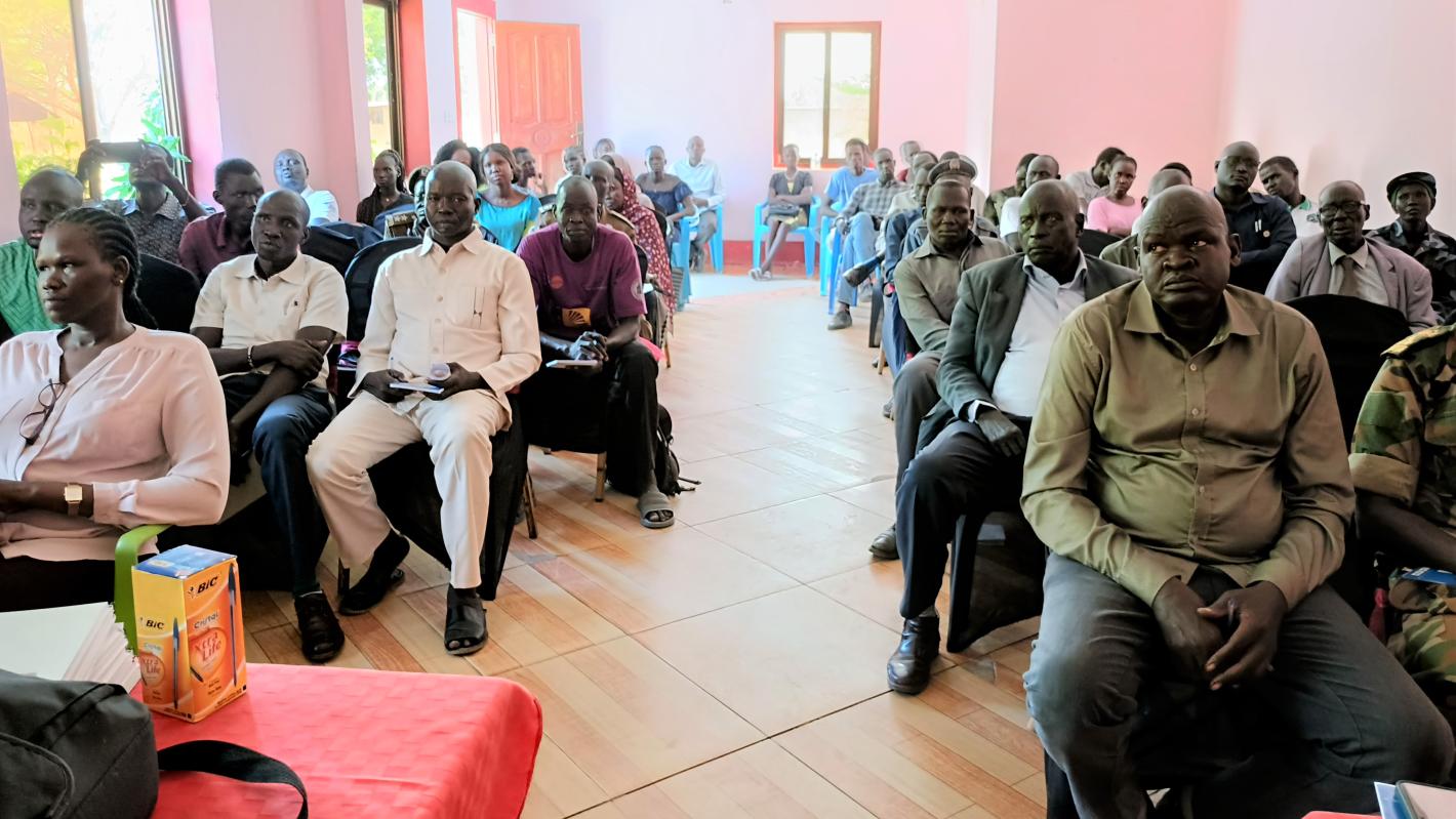 A room of people sitting in seats in rows with a aisle down the middle.