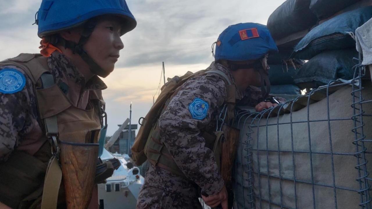 A close up photo of two Mongolian peacekeeper in their blue helmets and uniforms looking out from an outpost