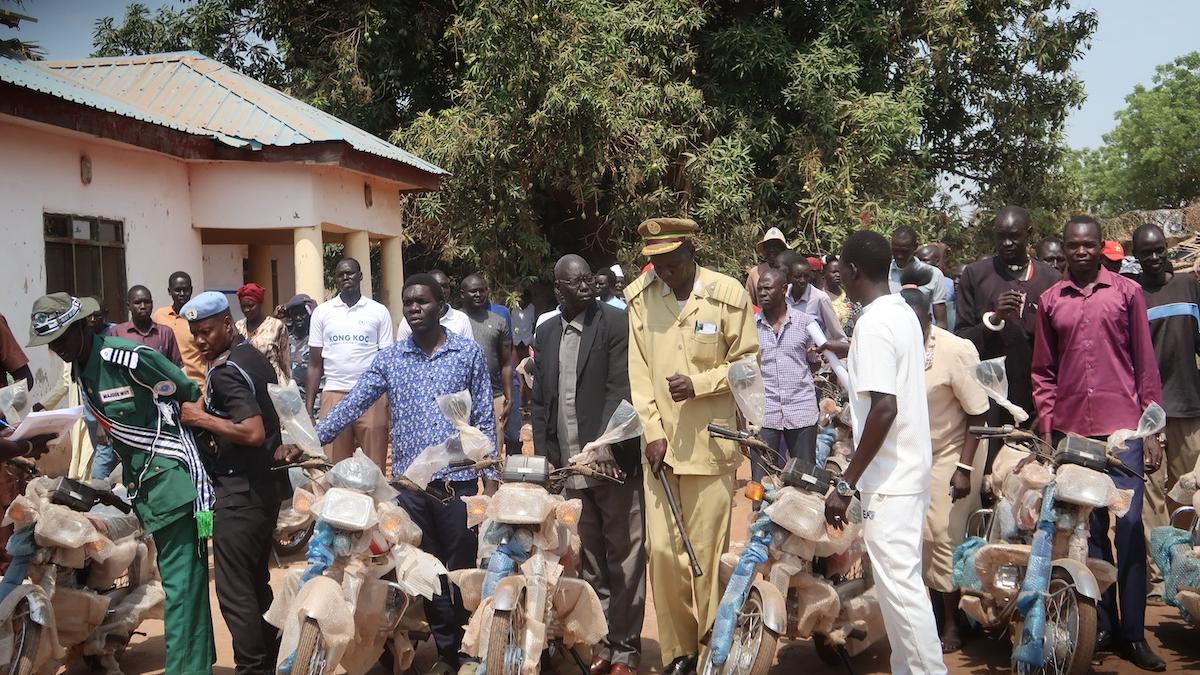 A group of people standing in a line holding motorbikes