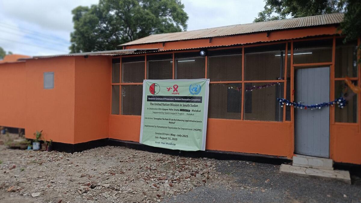 An orange building with a banner displaying information about a UN mission and HIV awareness program, with a door and windows visible and trees in the background.