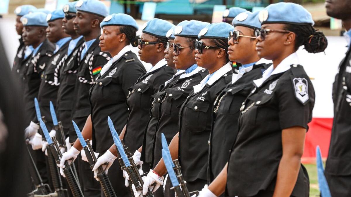 A line of uniformed UN police officers from Ghana in black attire and blue berets standing in formation, holding rifles with bayonets during a ceremonial event.