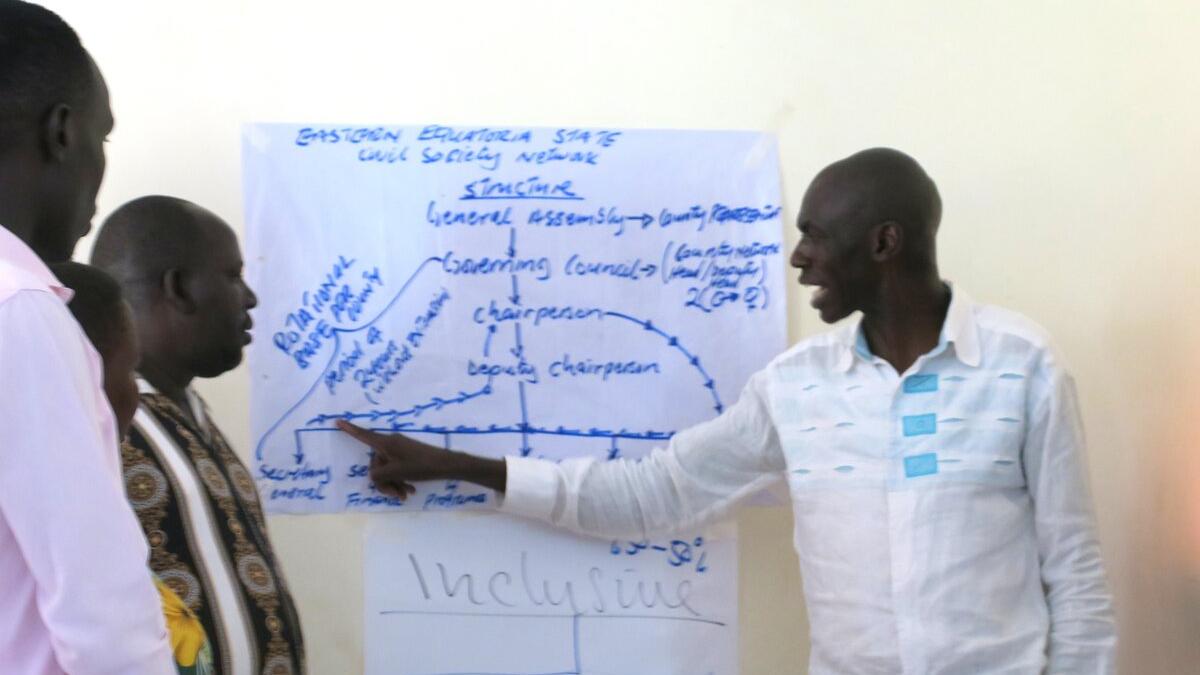 Members of the Civil Society Network in Eastern Equatoria developed a new action plan to boost engagement ahead of the country’s first elections as a sovereign state. Person pointing at a large sheet of paper with handwritten notes and diagrams during a group discussion, with others standing nearby.