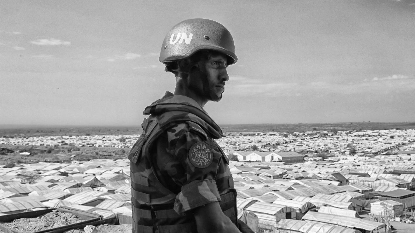 Black and white photo of a peacekeeeper surveilling buildings below.