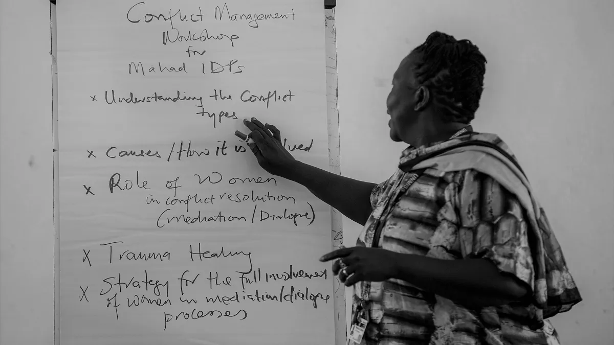 A black and white photo of a woman standing at a flipchart easel.