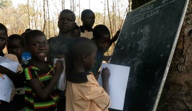 Under the branches of an ancient tree in Bazumburu, children gather together, excited and eager to hear the wise words of their teacher. Their only option for education is to attend lessons held out in the open air because their classrooms were destroyed