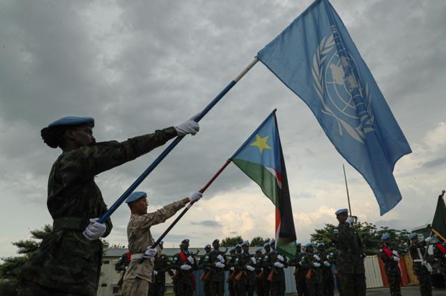 Two peacekeepers each holding a flag. One is holding the UN flag and the other is holding the South Sudanese flag.