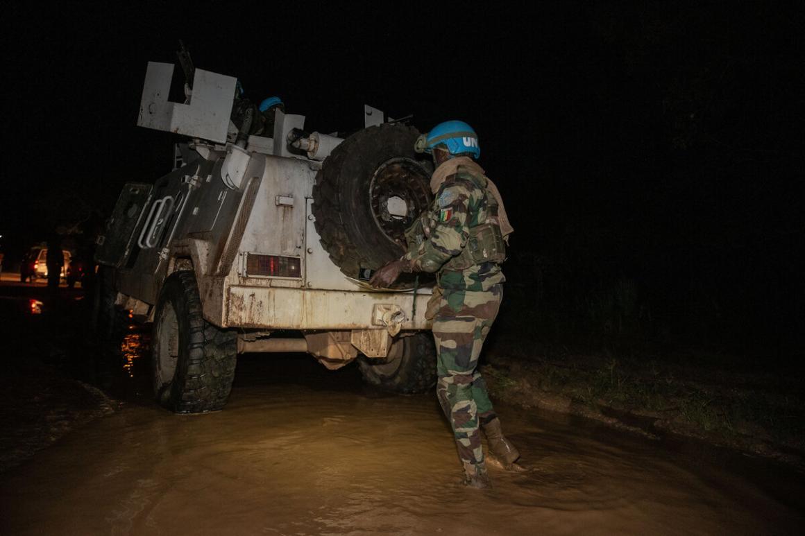 A peacekeeper wades through water behind a UN vehicle.